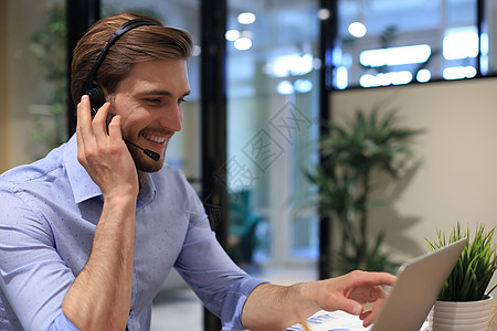 微笑的男性商业顾问戴着耳机坐在现代办公室 看着笔记本电脑屏幕进行视频通话 男士客户服务支持代理帮助热线在线聊天销售快乐联系助理关图片