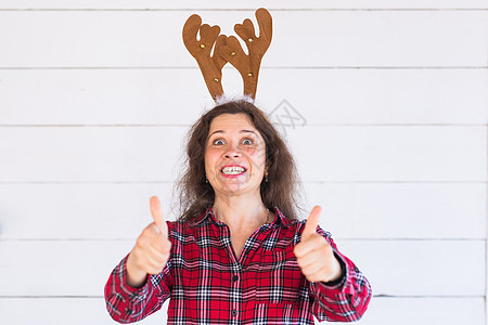 穿着圣诞服装的美丽快乐女人 头顶有鹿角 在白背景上用拇指摸着大拇指情绪牛角季节问候语面孔工作室眼睛女性女士微笑图片