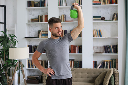英俊的男子在家里用小叮当做运动 健康生活的概念地面肌肉笔记本家庭客厅电脑健身房训练闲暇爱好图片
