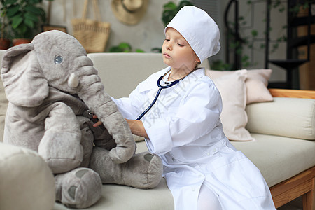 可爱的孩子打扮成医生 玩玩具大象 用听诊器检查它的呼吸情况医院儿科女性毛绒疾病童年职业衣服婴儿工作服图片