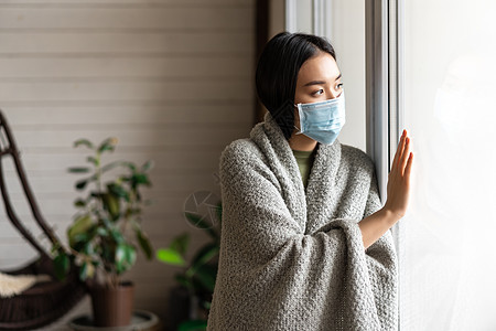 身戴着医疗面罩的生病的亚洲女孩站在窗边 渴望外出 被隔离 患19岁或感冒病鼻子疼痛温度肺炎窗户杯子痛苦毯子发烧房子图片