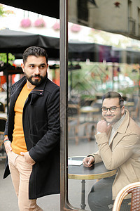 年轻时尚男子站在街上咖啡厅旁边的坐人附近图片