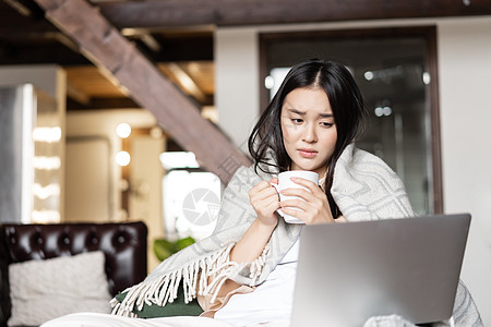 悲伤的亚洲女孩看着她的笔记本电脑 生病或感冒 喝杯茶等形象 远程教育 大流行病和检疫的概念流感微笑小憩闲暇假期房子家具学生椅子上背景图片