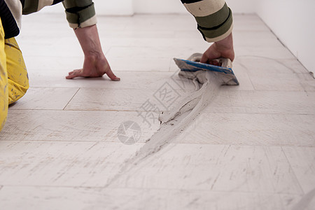 填满陶瓷木效应砖间间空间的提架男性工作建造关节地板装修瓷砖工人接缝石膏图片