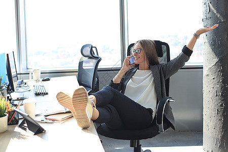 坐在现代办公室里 美丽的女商务人士正在用手机聊天 微笑着情绪地点生活方式休闲快乐经理幸福谈判工作创造力图片