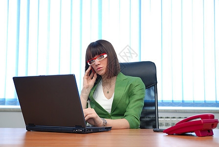 年轻女商务人士在办公室用笔记本电脑工作商业电话人士秘书商务桌子互联网代理人女性服务图片