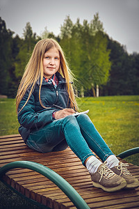 金发女孩在春天写了一封信 坐在公园的一根木条长裙上图片