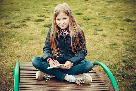一位在春天的学龄女孩坐在林区一个木制长裙上写了一封信图片