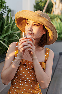 美丽的亚洲女孩坐在长椅上 在夏日阳光下喝果汁运动女士假期女性食物饮食裙子帽子营养闲暇图片