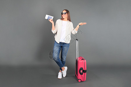 穿暑期散装的年轻旅游女孩 有太阳镜 红色手提箱 护照 机票和孤立的灰色背景行李树干案件旅行闲暇女士旅游手提包休息商业图片