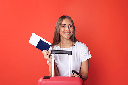 穿暑期散装的年轻旅游女孩 带着太阳镜 红色手提箱 在红色背景下被孤立的护照树干女性女孩商业文档手提包冒险飞机场行李案件图片