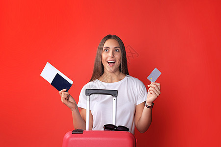 穿暑期散装的年轻旅游女孩 带着太阳镜 红色手提箱 在红色背景下被孤立的护照女士航程航空公司假期飞机场旅游游客树干案件冒险图片