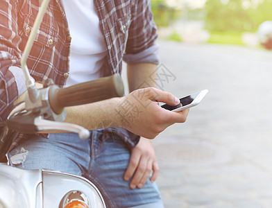 坐在摩托车上并使用智能手机的年轻人电话技术假期反射运输摄影青年晴天屏幕手表图片
