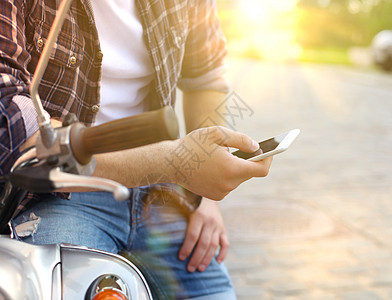 坐在摩托车上并使用智能手机的年轻人电话晴天游客工具假期摄影运输潮人手表皮肤图片