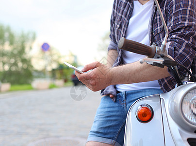 坐在摩托车上并使用智能手机的年轻人运输晴天手表男人天空游客反射潮人假期屏幕图片