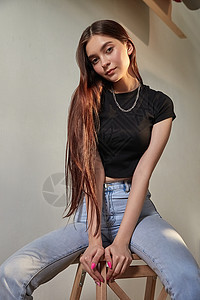 坐在木凳上穿着牛仔裤长头发的年轻caucasia女孩肖像图片