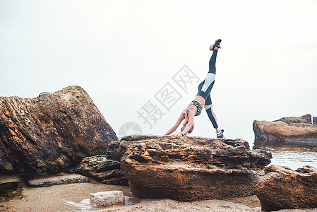 早上练瑜伽 身穿运动服 假腿站立在海边的石头上做瑜伽的健康和运动残疾女运动员图片
