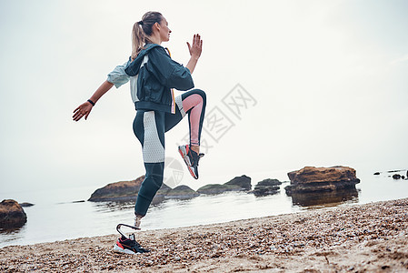 每天早上都锻炼运动 对有假肢的年轻运动残疾妇女的侧视正在海滩上进行体育锻炼图片