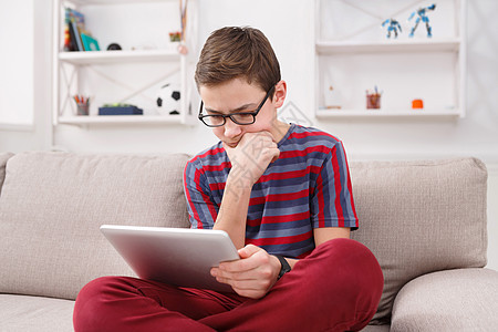 少年男孩在家里沙发上使用数字平板电脑电子长椅手表技术药片男性网络青少年家庭作业视频图片