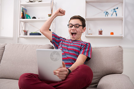 在家中沙发上使用数字平板电脑的少年男孩教育技术闲暇药片触摸屏孩子足球电子家庭作业手表图片