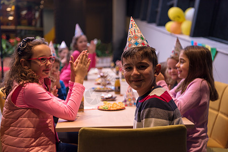 年轻男孩欢喜地庆祝他的生日孩子气球帽子快乐微笑童年桌子气氛情感庆典图片