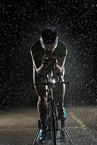 在雨夜快速骑着自行车的三亚马龙运动员活力赛车手黑色铁人天气钢铁侠男人头盔训练运动图片