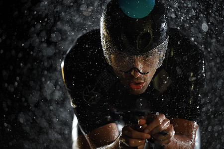 在雨夜快速骑着自行车的三亚马龙运动员运动天气赛车手男人速度活力训练钢铁侠头盔铁人图片