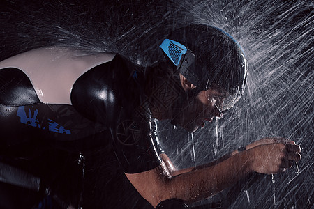 在雨夜快速骑着自行车的三亚马龙运动员行动头盔钢铁侠运动训练男人铁人速度竞赛天气图片