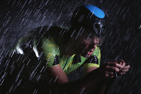 在雨夜快速骑着自行车的三亚马龙运动员竞赛天气耐力活力训练头盔钢铁侠运动男人黑色图片