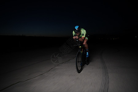 夜里快速骑自行车的三重运动员健康活力凝胶黑色行动竞赛速度钢铁侠耐力铁人图片