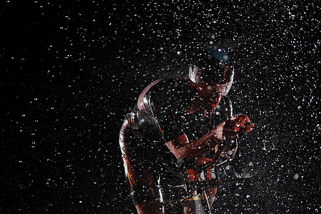 在雨夜快速骑着自行车的三亚马龙运动员天气活力钢铁侠头盔铁人耐力男人赛车手黑色竞赛图片