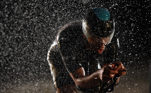 在雨夜快速骑着自行车的三亚马龙运动员赛车手钢铁侠黑色天气竞赛行动速度耐力活力运动图片