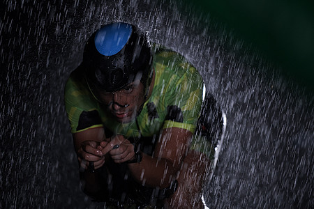 在雨夜快速骑着自行车的三亚马龙运动员赛车手竞赛耐力行动天气钢铁侠活力速度运动铁人图片