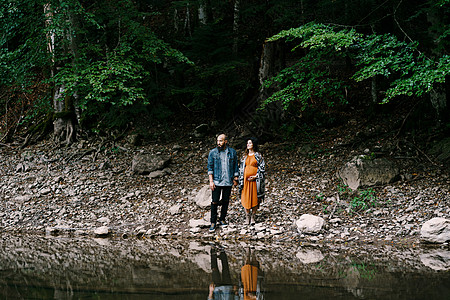 与男子同孕的孕妇站在一个岩石斜坡上 湖边环绕着树木图片