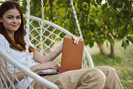 穿着膝上型笔记本的吊床露天快乐的女人自由职业者阅读公园热带旅行花园假期工作海滩丛林图片