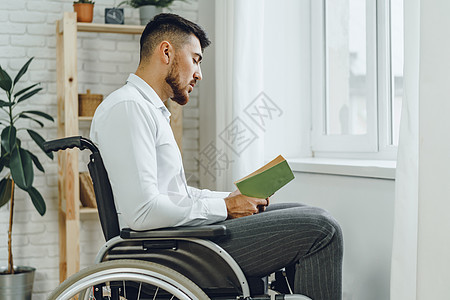 残疾人在轮椅上阅读室内书籍的残疾男子学生工作房子男人放松残障人士思维学习闲暇背景图片