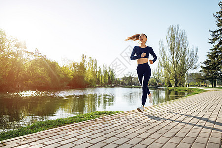 运动健壮的年轻女子清晨在公园慢跑运动装赛跑者跑步锻炼树木女士行动运动员阳光慢跑者图片