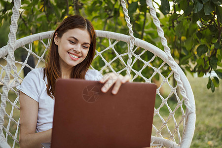 带有膝上型电脑技术的吊床露室内微笑的妇女公园海滩上网花园女性自由职业者屏幕工作假期旅行图片