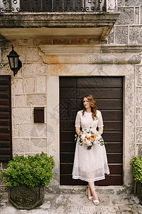 在一栋旧石屋门前用花架站立着的新娘图片
