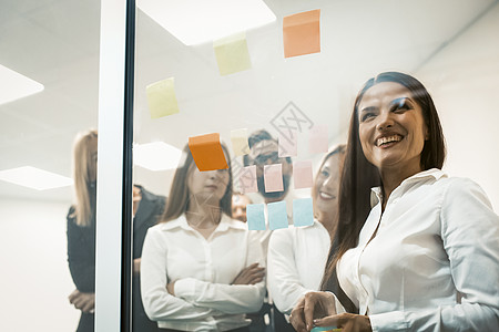 一群年轻的商务人士使用多色贴纸将它们贴在玻璃墙上 在创意办公室一起研究想法和交流 一个成功的队概念图片