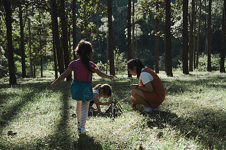 母亲和两个女儿在森林露营地收集柴火和点燃篝火 家人和孩子们在大自然的树林里生篝火 家庭露营 一起度假童年女孩关爱娱乐教育兄弟营火图片