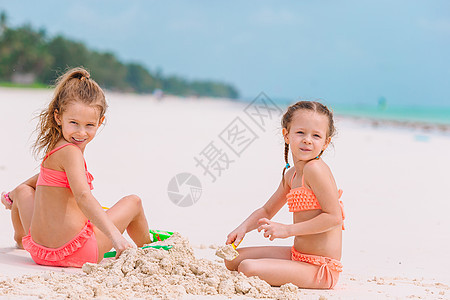 在沙滩上暑假期间 可爱的小姑娘们孩子快乐闲暇女孩玩具沙堡热带裙子海滩海岸图片