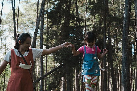 年轻母亲帮助她的女儿在公园的木头上行走 孩子在平衡梁上 游戏是在童年学习娱乐院子运动教育闲暇假期享受女孩快乐草地图片