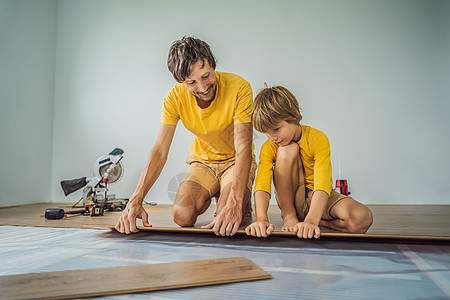 父亲和儿子在温暖的薄膜地板上安装新的强化木地板 复合地板下的红外线地暖系统工具微笑活力装潢锤子工人技术装修维修男人图片
