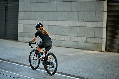 白天在户外训练时穿黑色自行车服和防护装备骑自行车的专业女自行车手的后视图图片
