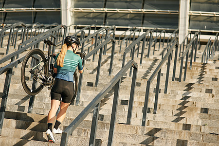 职业女自行车手穿着自行车服和护具的全长镜头 肩上骑着自行车走上台阶 在户外训练图片