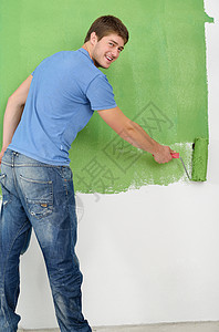 英俊的青年男子用彩色漆白白墙滚筒工匠男性装潢蓝色刷子画家房间装修房子图片