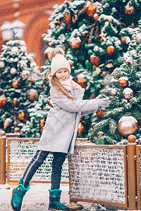 新的一年 在雪地的fir tree树枝附近的小快乐女孩城市女孩女儿手套市场帽子幸福童年街道枞树图片