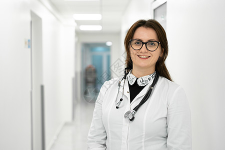 自信微笑的年轻女医生站在医疗机构 戴着眼镜的骄傲的专业医生治疗师女人在医院走廊里看着相机 全科医生的肖像医师冒充女性卫生风镜快乐图片