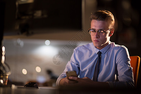 男子在暗办公室使用移动电话阅读商业员工桌子人士技术工作设计师屏幕办公室图片